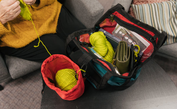 A person knitting out of a Yarn Stuff Sack with a full Little Swift opened beside it.